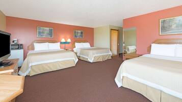 A hotel room with three beds, a television, a desk, and a microwave.