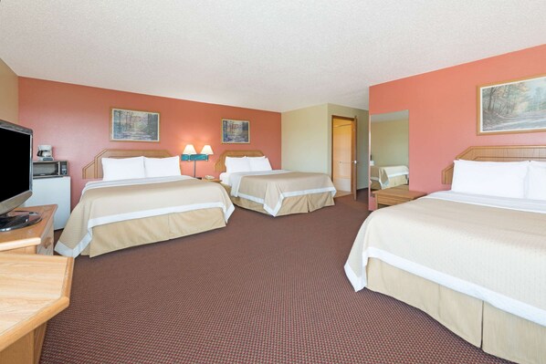 Quarto de hotel com três camas, televisão, secretária e micro-ondas.