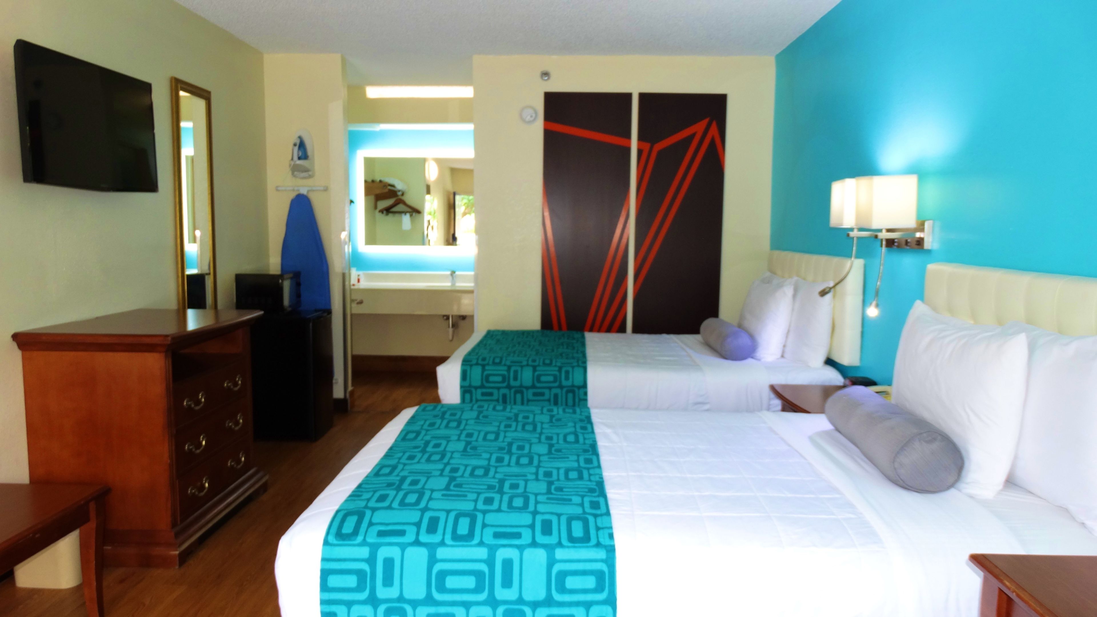 A hotel room with two beds, a dresser, a mirror, a TV, and a bathroom visible through an open door.