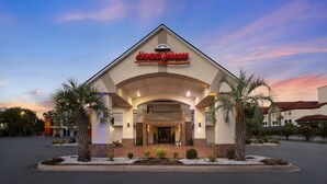Et Howard Johnson hotel med et tydeligt skilt, en overdækket indgang og en anlagt forhave med palmer.