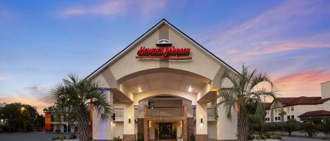 Un hotel Howard Johnson con un letrero llamativo, un acceso cubierto y un frente ajardinado con palmeras.