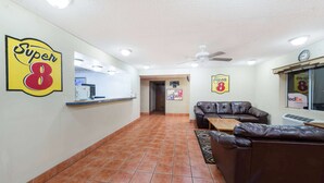 A lobby with a reception desk, a sofa, a ceiling fan, and a wall with 'Super 8' signage.