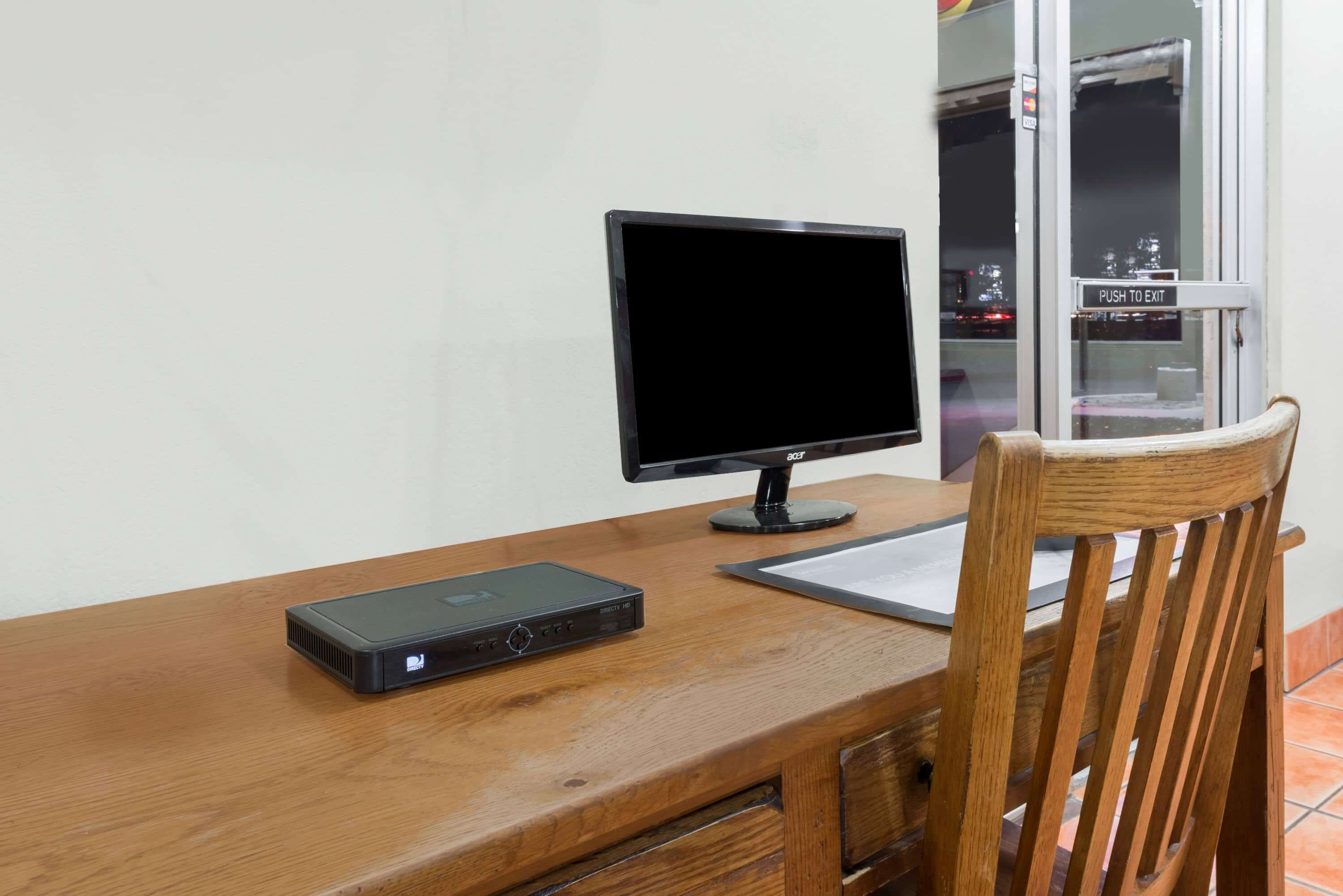 A wooden desk with a computer monitor, a keyboard, and a small electronic device.