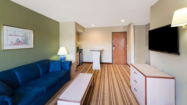 A hotel room with a blue sofa, a small table, a cabinet, a TV, and a painting on the wall.