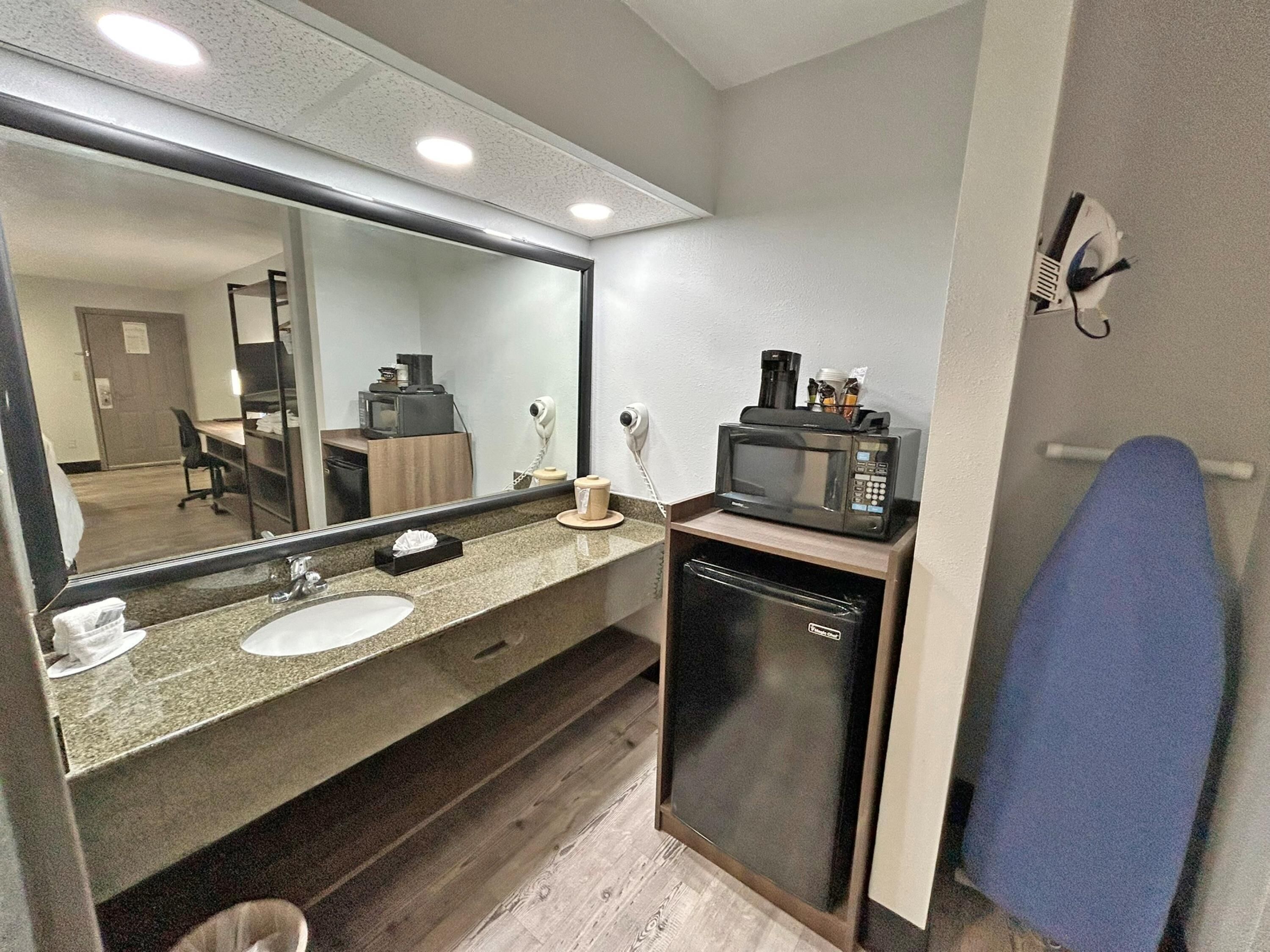 Casa de banho com lavatório, espelho, micro-ondas e porta-toalhas.
