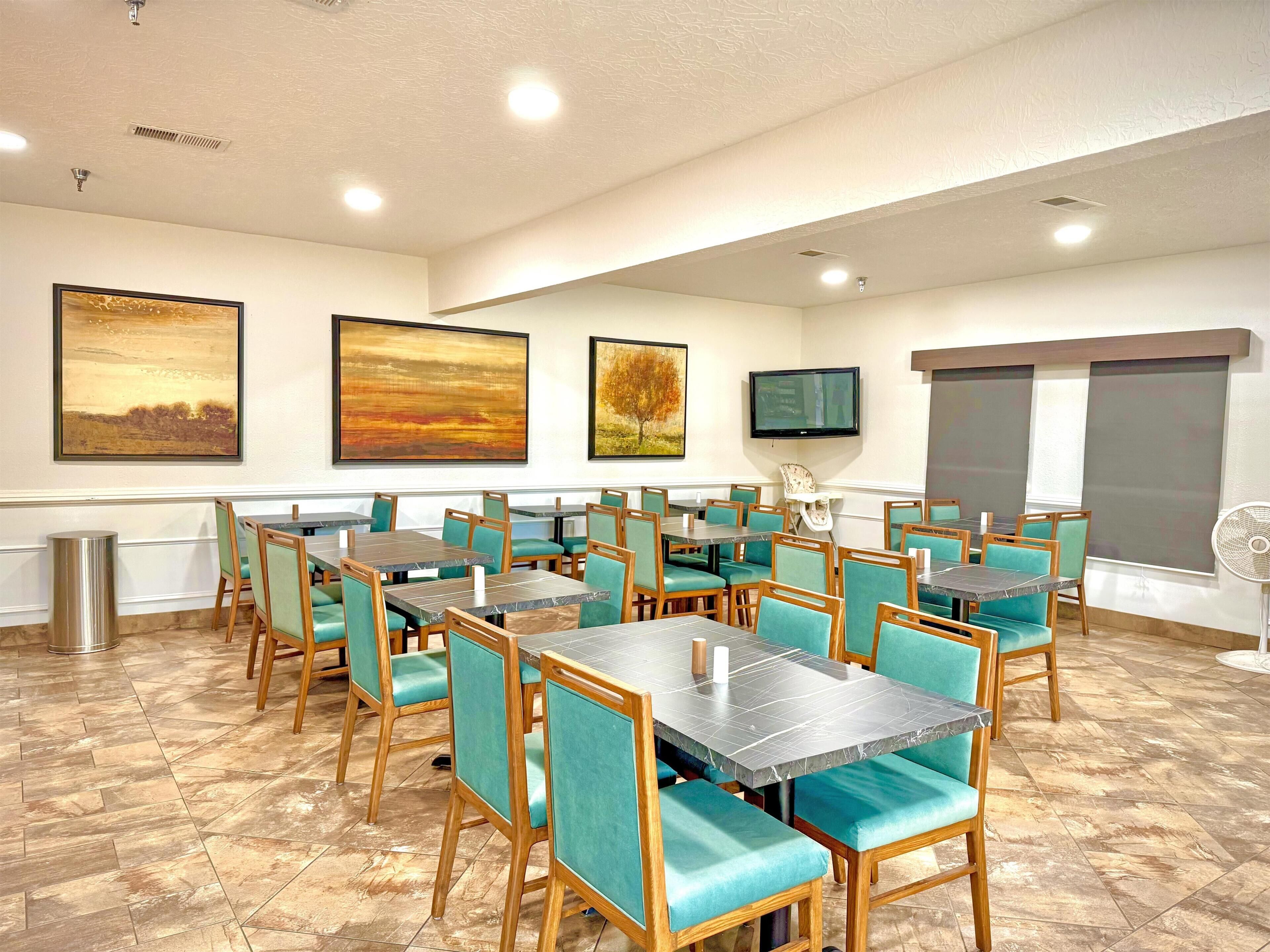 Un comedor de hotel con varias mesas y sillas, un televisor y obras de arte en las paredes.