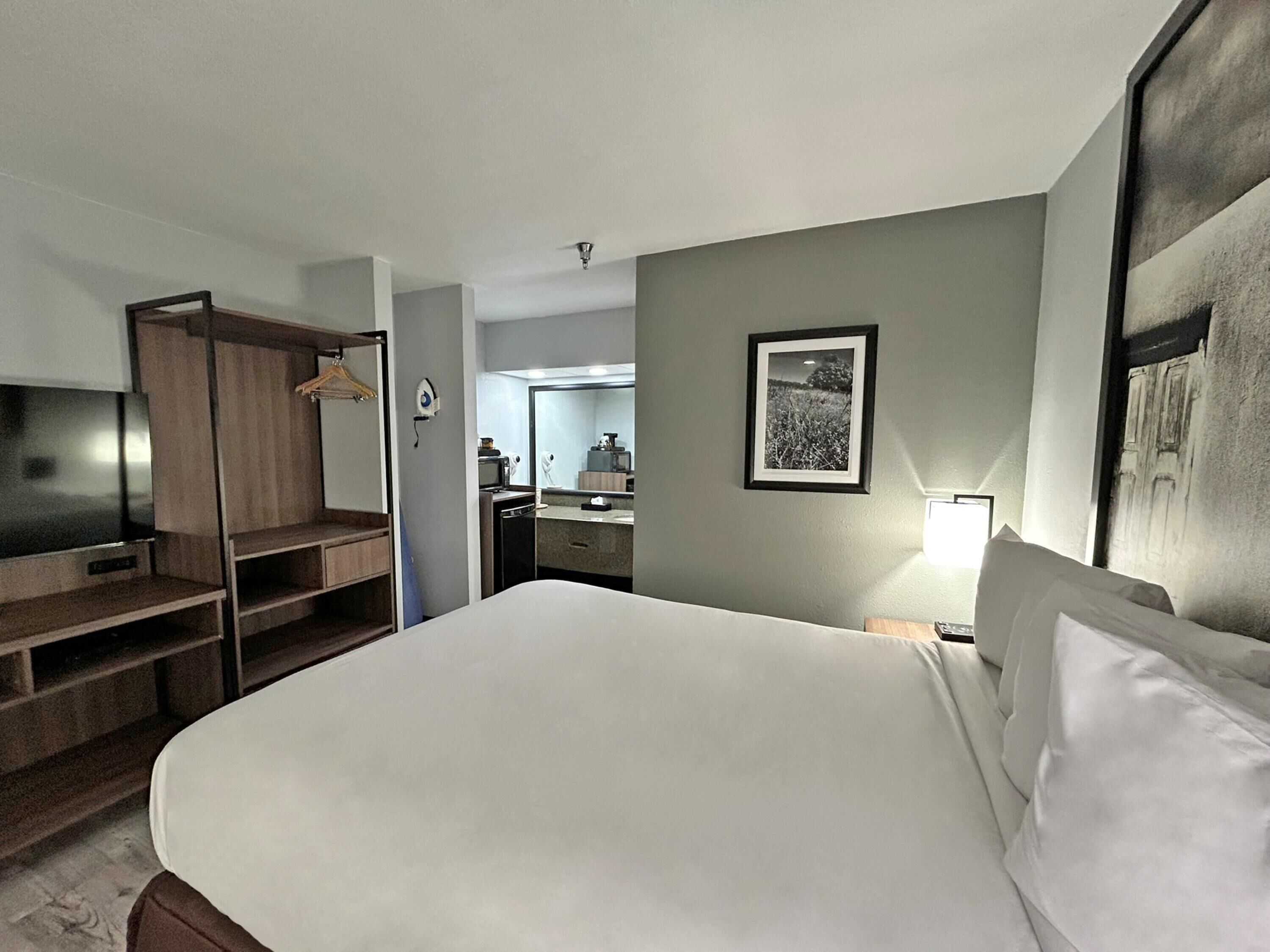 A hotel room with a bed, a wardrobe, a desk, a mirror, and a framed picture on the wall.