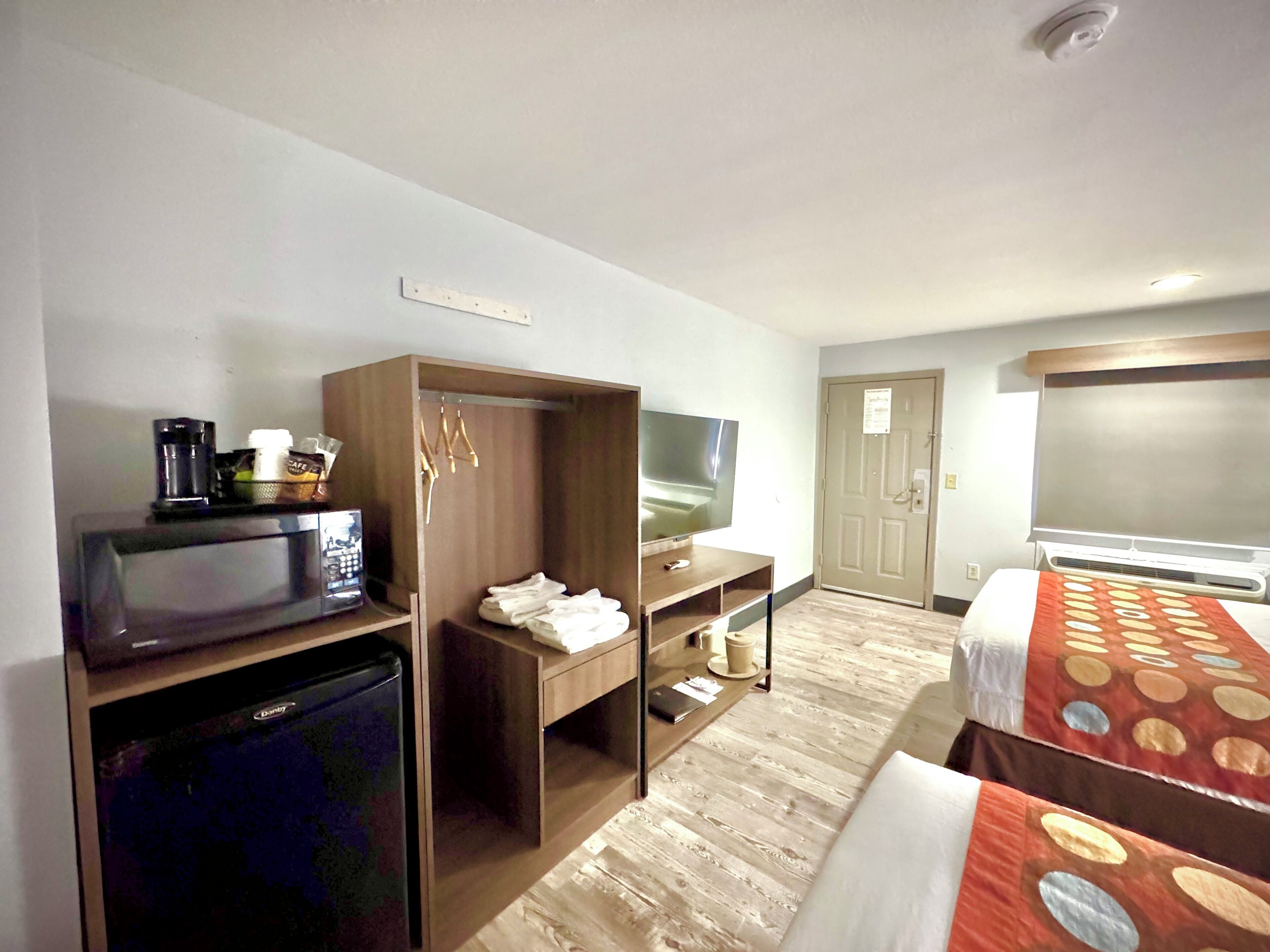 Ein Hotelzimmer mit Bett, Fernseher, Kleiderschrank, Mikrowelle und kleinem Kühlschrank.