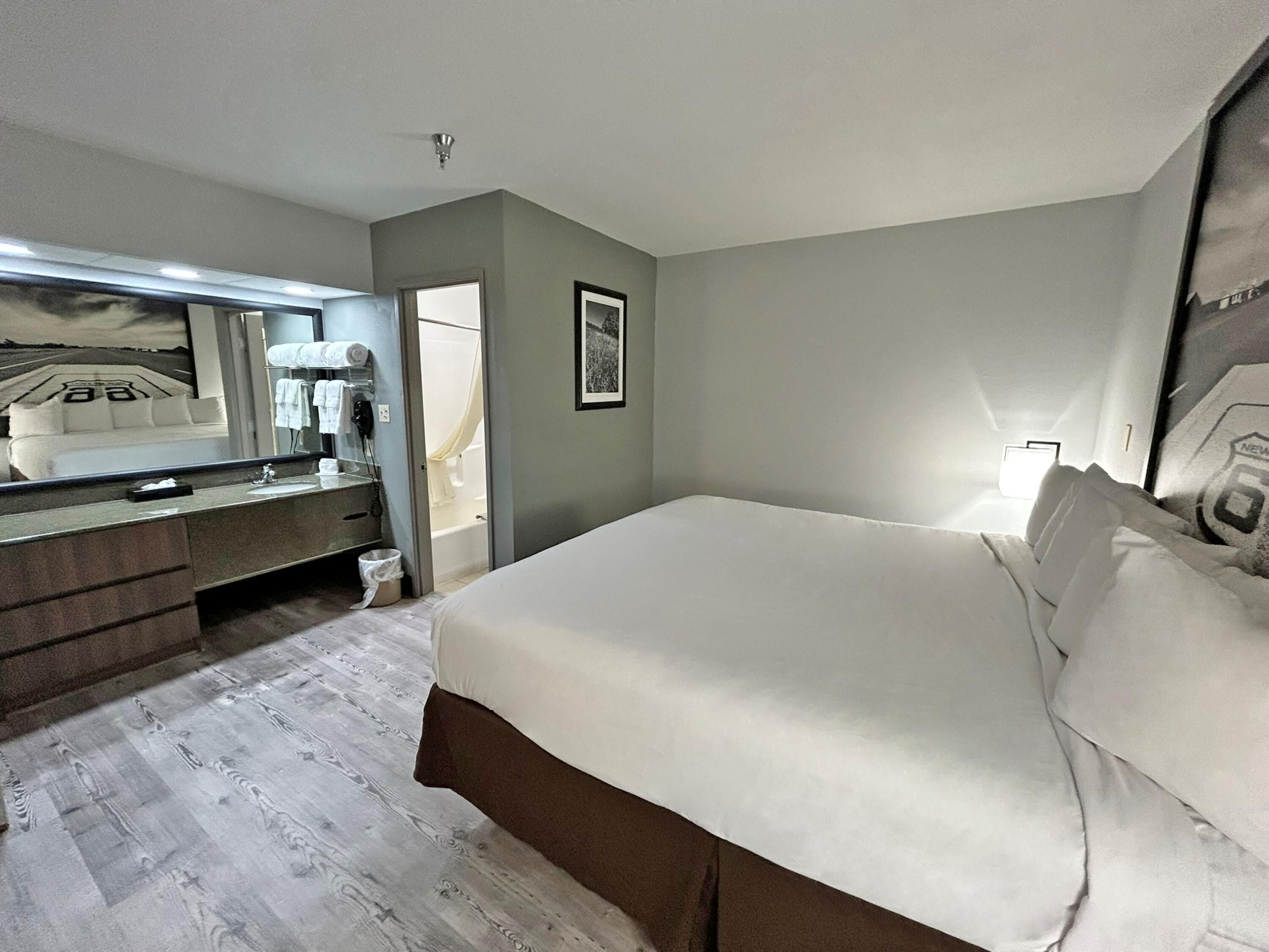 A hotel room with a bed, a dresser, a mirror, and a bathroom visible through an open door.