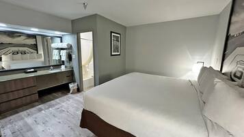 A hotel room with a bed, a dresser, a mirror, and a bathroom visible through an open door.