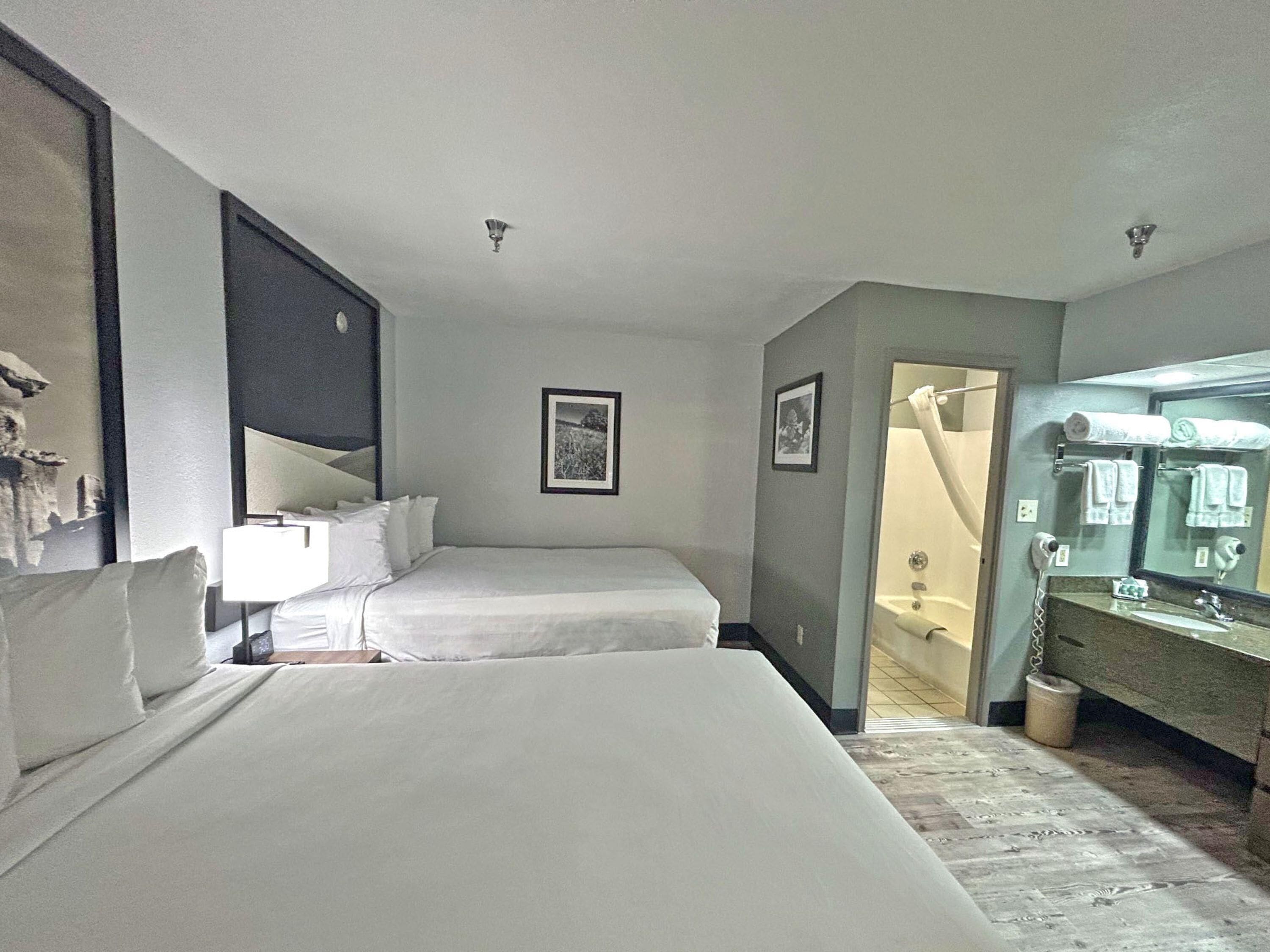 A hotel room with two beds, a bathroom with a mirror and towel rack, and a framed picture on the wall.