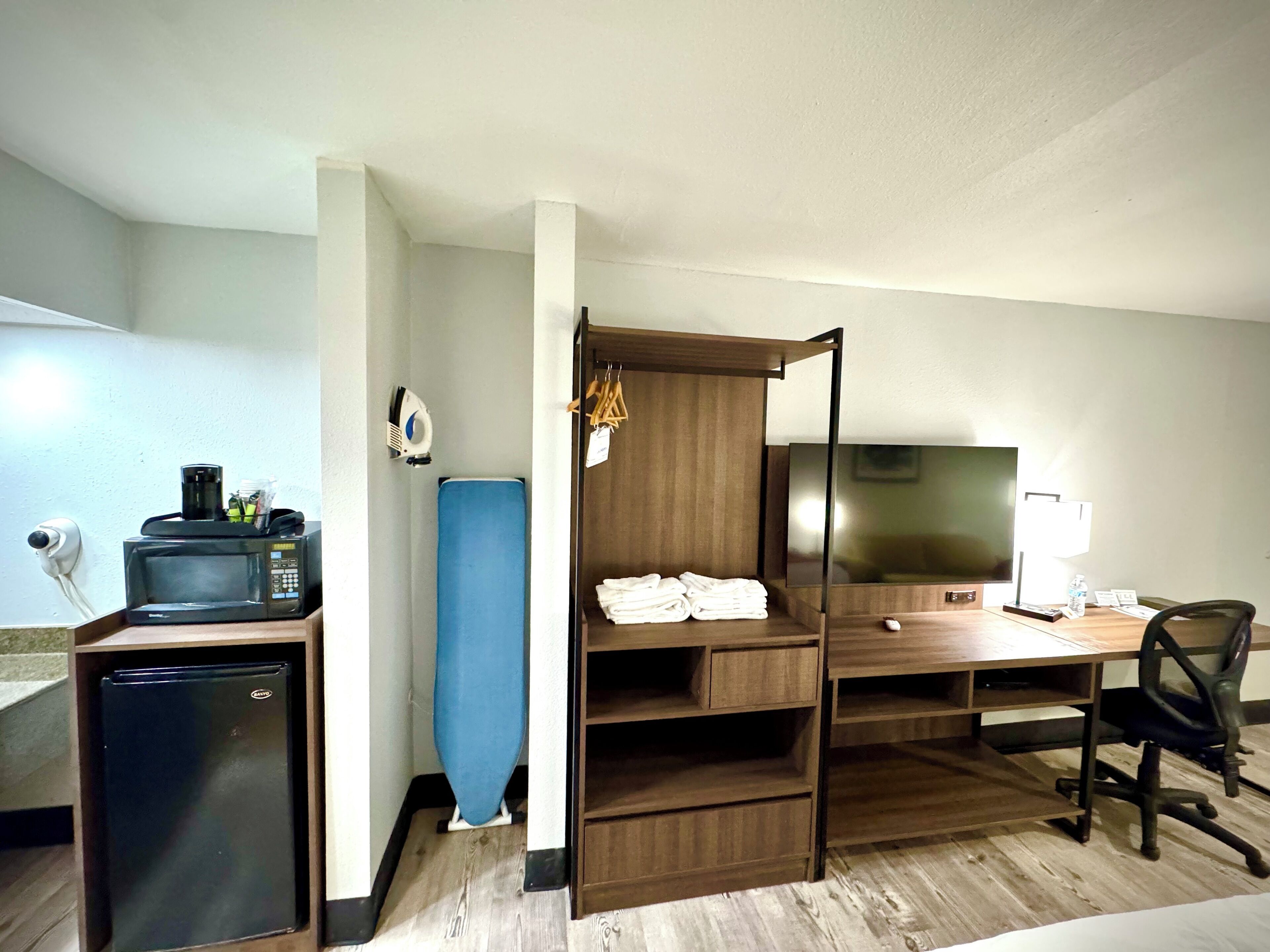 Une chambre d’hôtel compacte équipée d’une kitchenette, d’un bureau, d’une chaise, d’une télévision et d’une armoire.