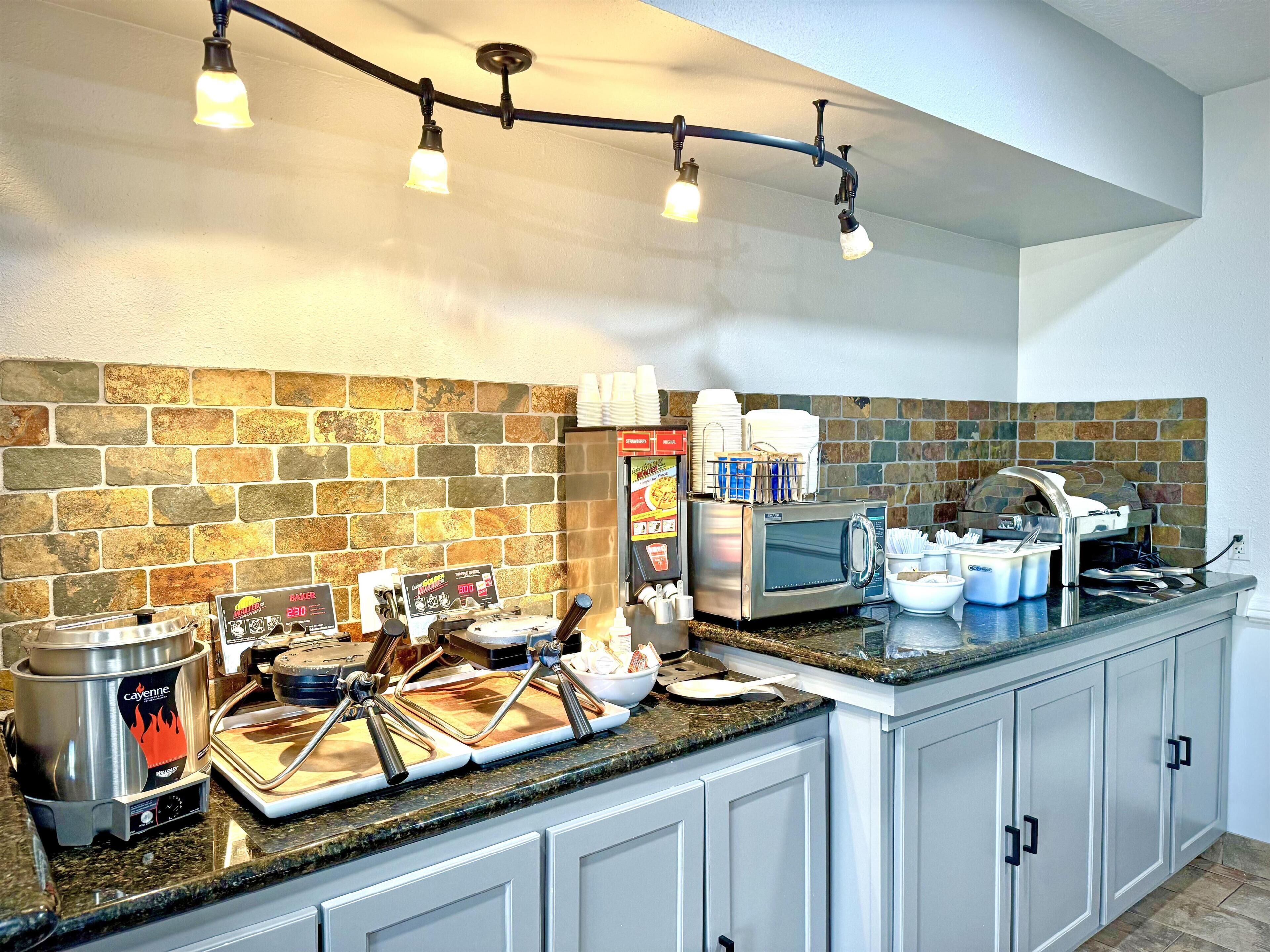 A commercial kitchen with a stone backsplash, a coffee machine, and a buffet setup.