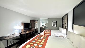 Habitación de hotel con cama, escritorio, silla, televisor y espejo.
