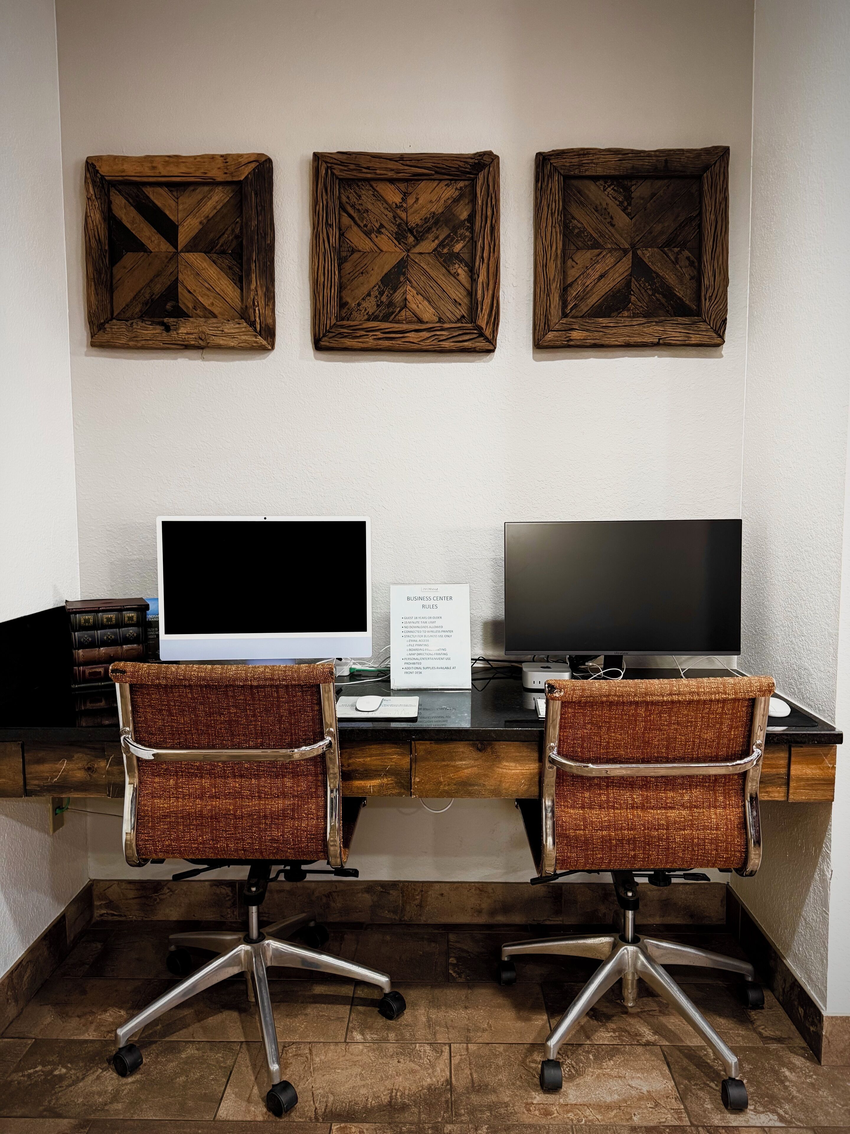 Un centro de negocios con dos sillas de oficina, un escritorio con dos monitores y tres adornos de pared de madera.