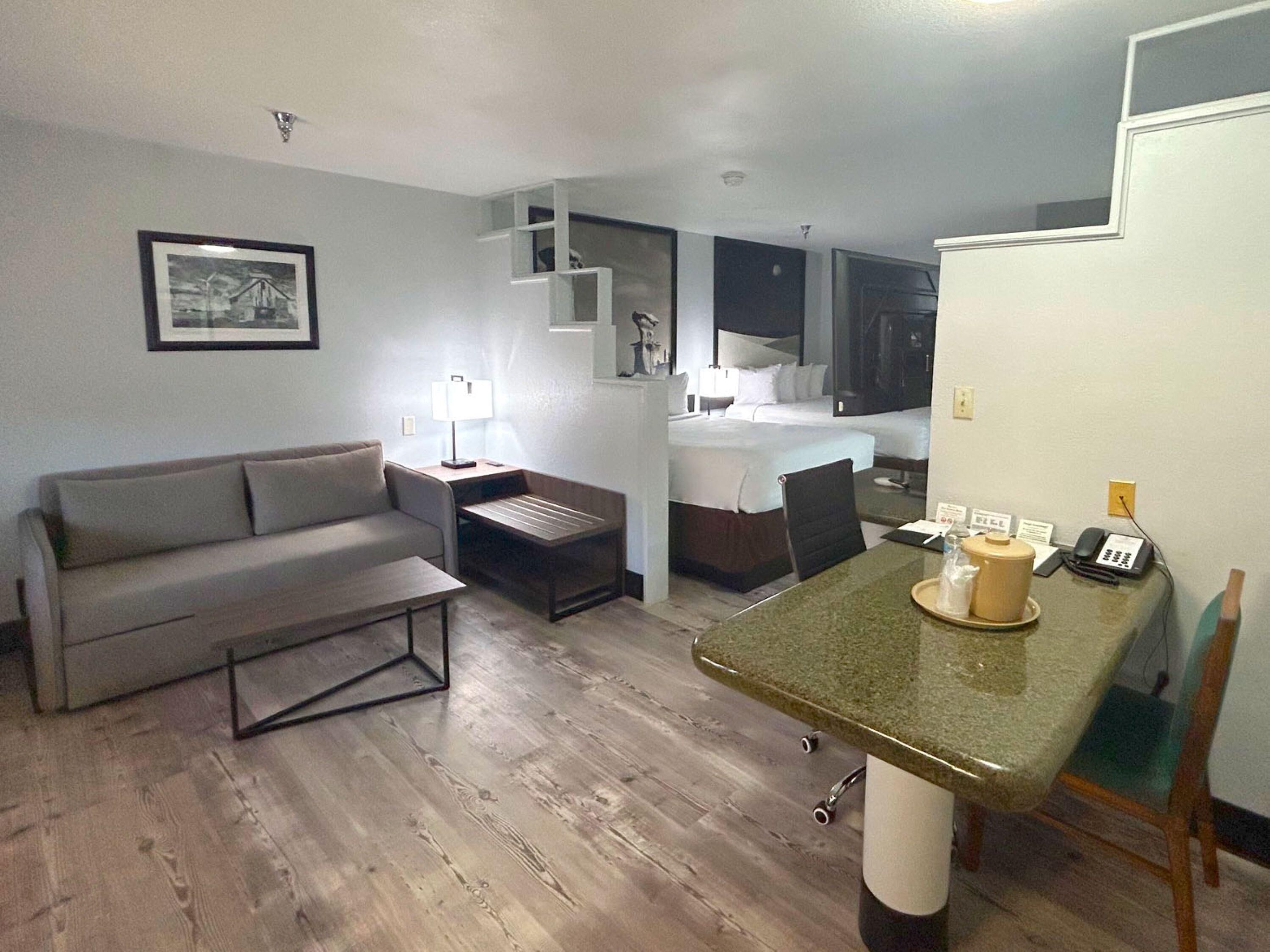 Habitación de hotel compacta con sofá, una pequeña mesa de comedor, cama y escritorio con lámpara.