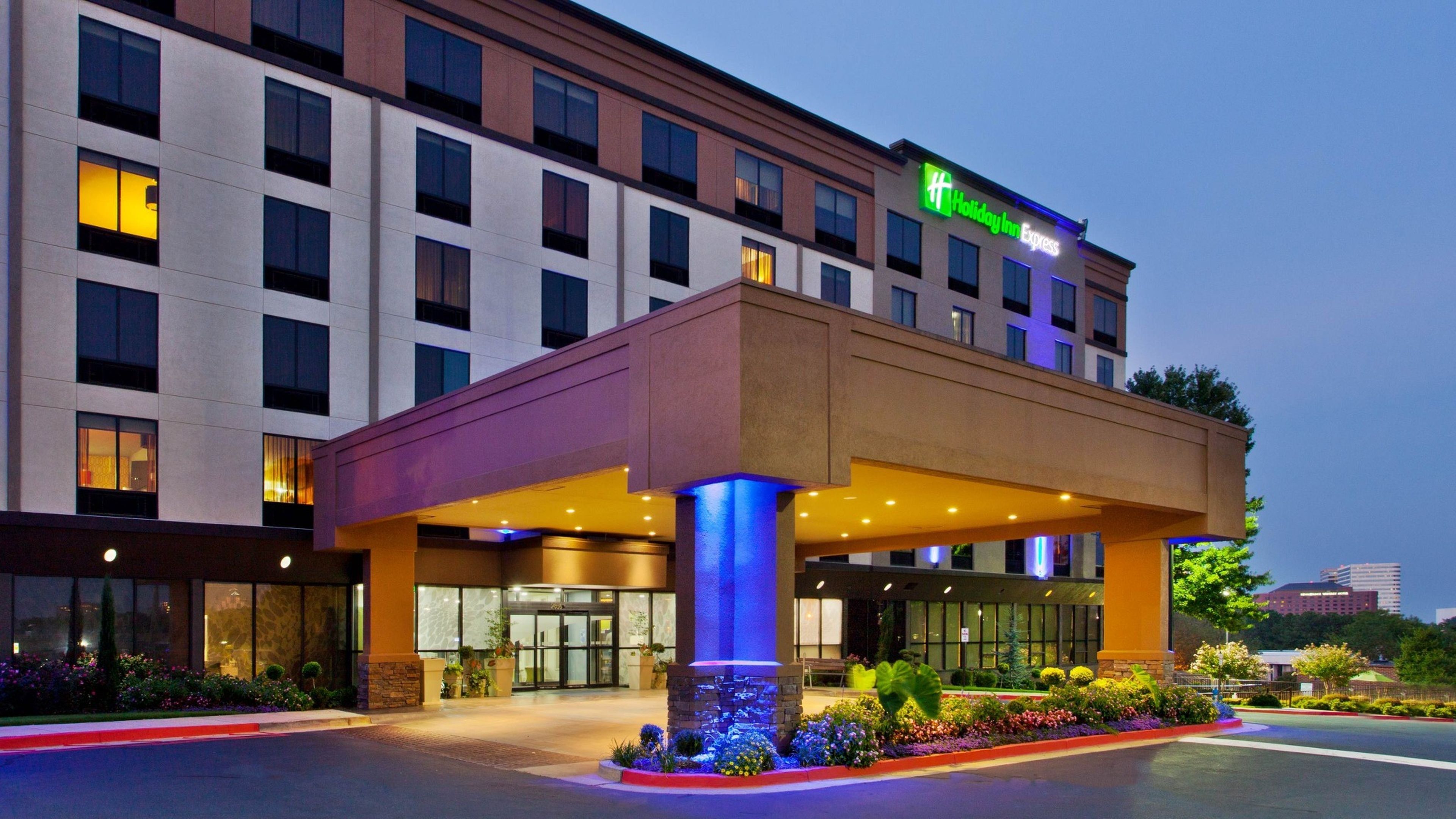 Un hotel Holiday Inn Express con entrada cubierta, iluminación exterior y un jardín paisajístico.