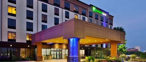 Un hotel Holiday Inn Express con entrada cubierta, iluminación exterior y un jardín paisajístico.