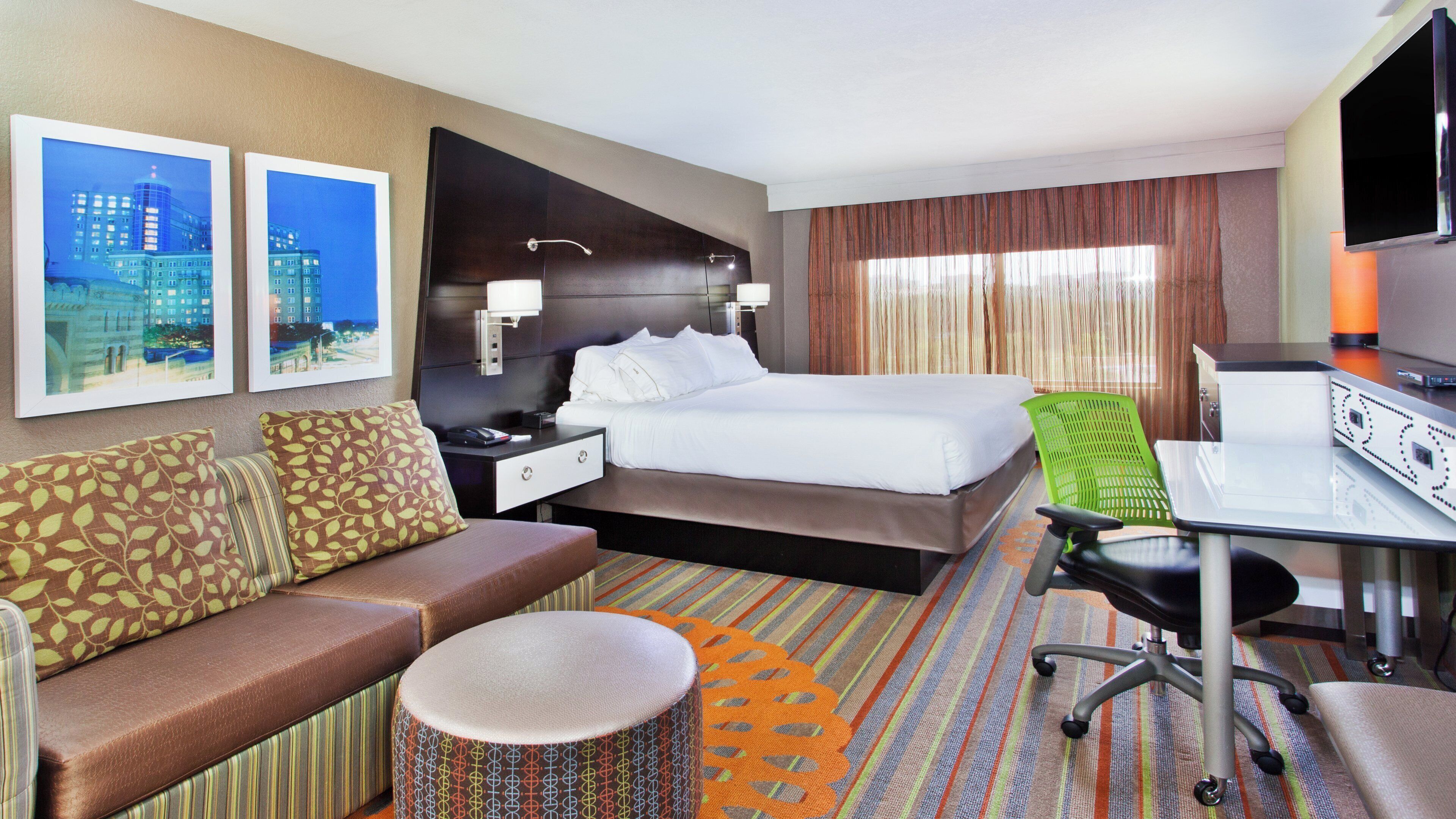 Una habitación de hotel con una cama, un escritorio con una silla, un sofá y un otoman redondito.