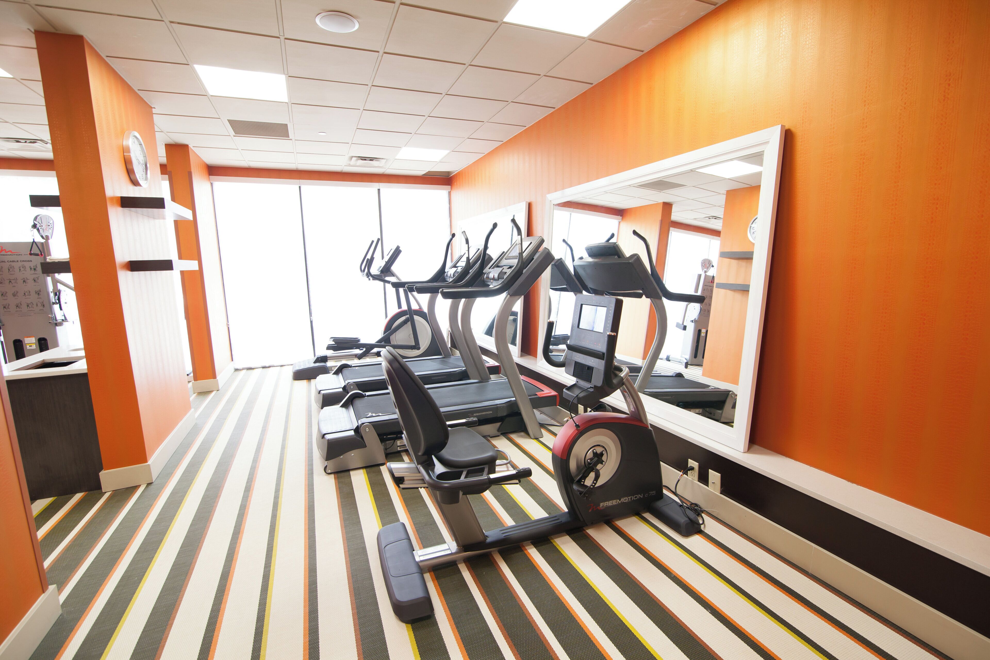 Un gimnasio con cintas de correr, una bicicleta estática y un espejo grande.