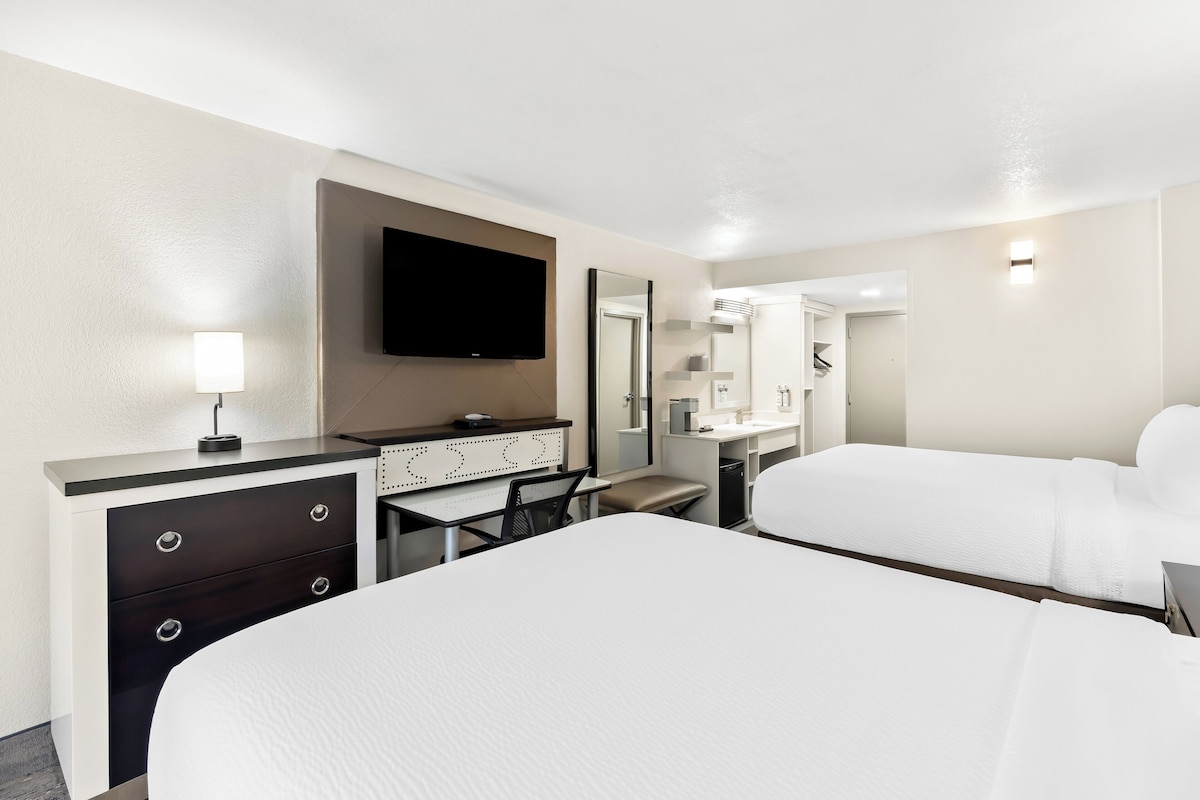 A hotel room with a large bed, a desk with drawers, a flat-screen TV, a mirror, and a bathroom visible through an open door.