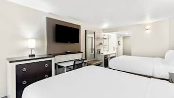 A hotel room with a large bed, a desk with drawers, a flat-screen TV, a mirror, and a bathroom visible through an open door.