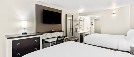 A hotel room with a large bed, a desk with drawers, a flat-screen TV, a mirror, and a bathroom visible through an open door.