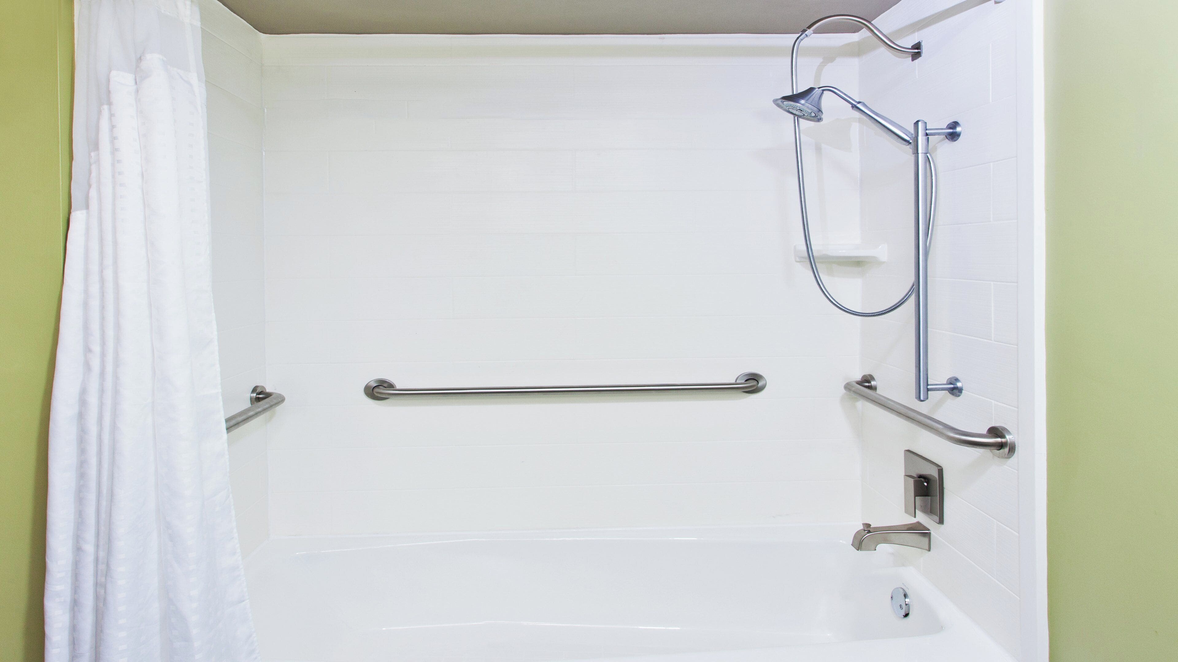 A bathroom with a white bathtub, grab bars, a shower head, and a curtain.