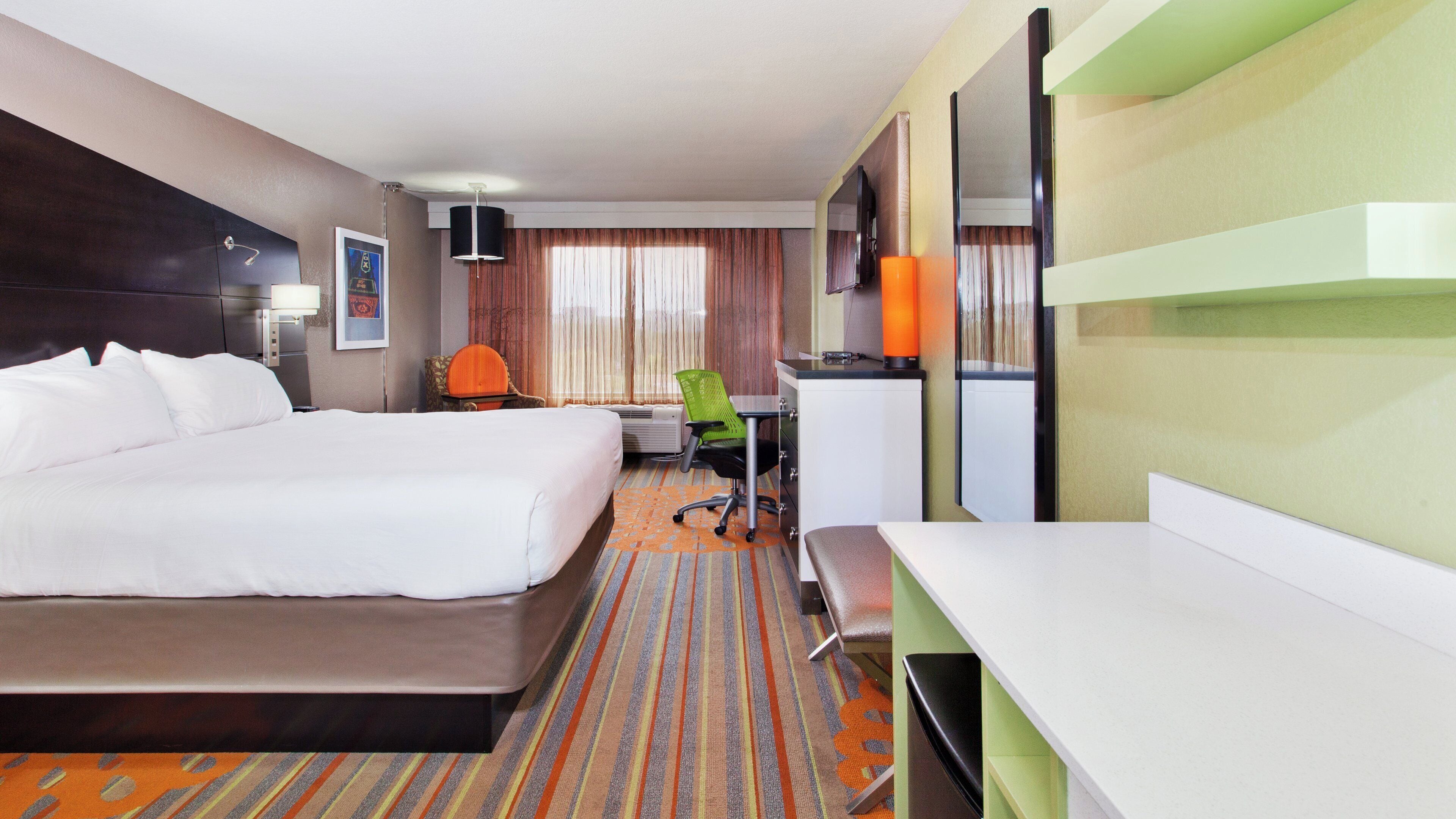 A hotel room with a bed, desk, chair, and a television.