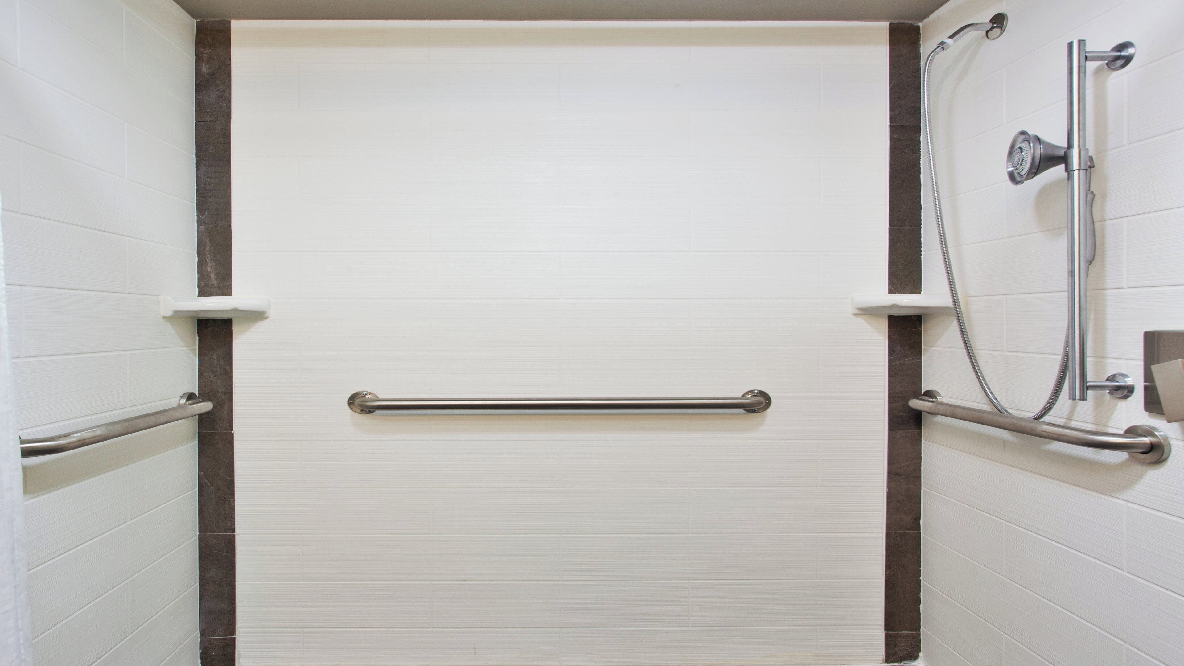 A bathroom with white tiled walls, a door with a handle, and a shower area with a handheld showerhead and a handheld shower hose.