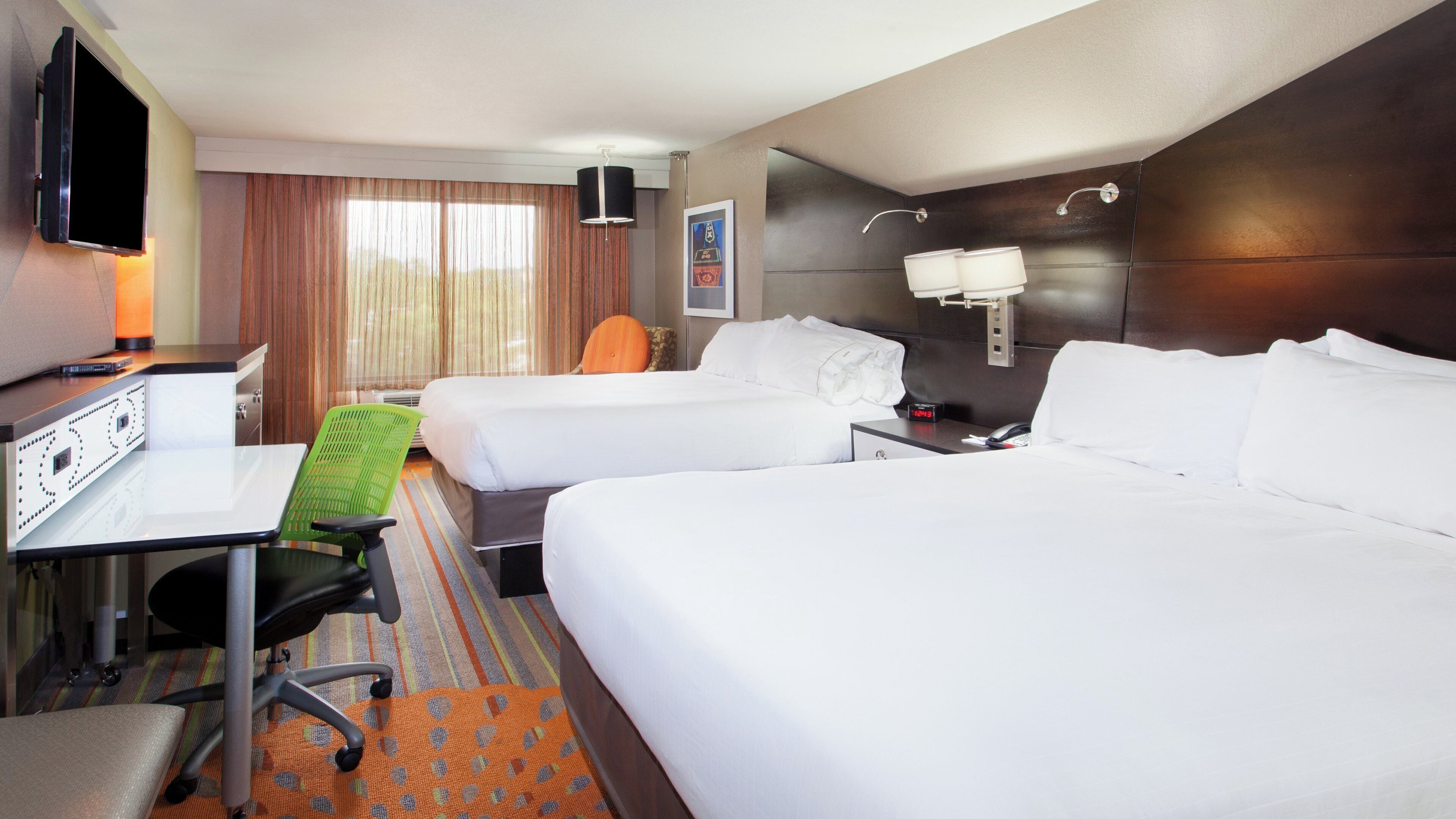 Een hotelkamer met twee bedden, een bureau met een computer, een stoel en een televisie.