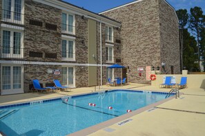 A swimming pool with blue tiles, surrounded by a brick building with multiple windows and blue lounge chairs. - Comfort Inn Savannah Midtown (Savannah)