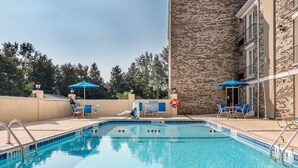 A swimming pool with blue tiles, surrounded by lounge chairs and umbrellas, with a brick building in the background. - Comfort Inn Savannah Midtown (Savannah)
