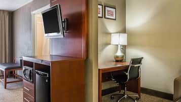 A hotel room with a wooden desk, a chair, a television mounted on the wall, a lamp, and a bed.