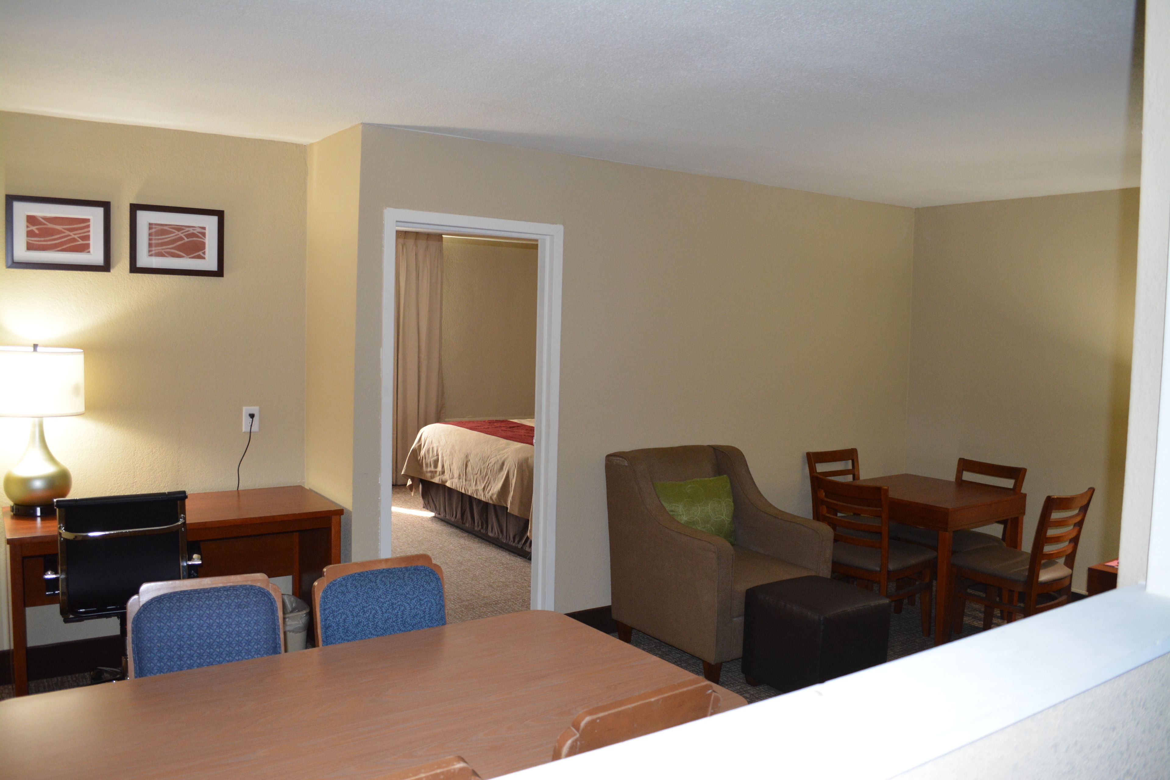 A hotel room with a bed, a desk with a lamp, a dining area with chairs, and a small table.