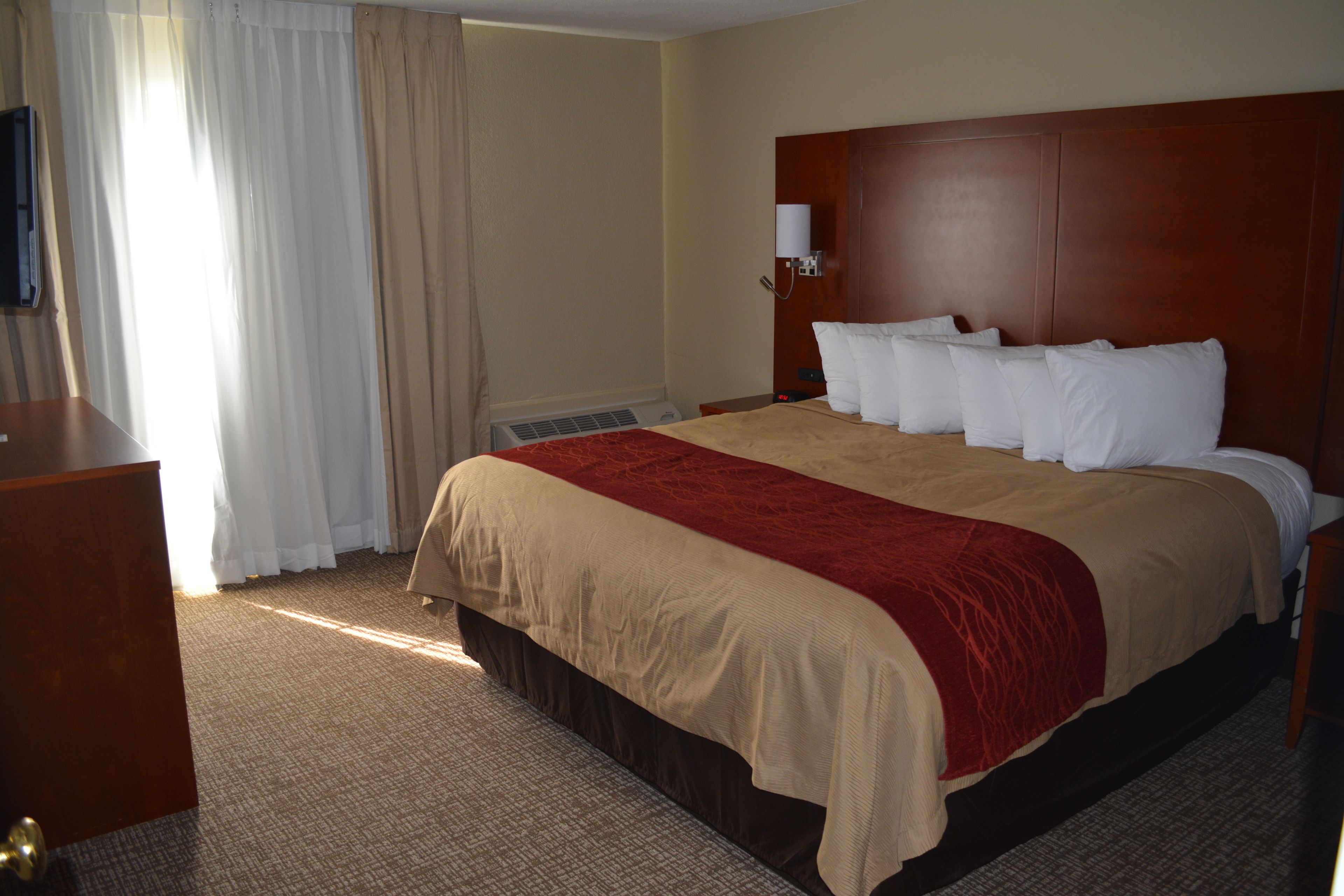 Une chambre d’hôtel avec un grand lit, une tête de lit en bois, un téléviseur à écran plat et un bureau avec une chaise.