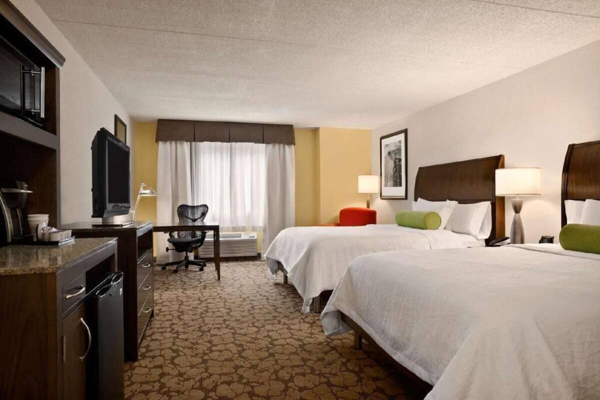 A hotel room with two beds, a desk, a television, and a chair.