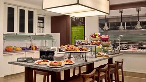 A modern kitchen with a central island, bar stools, and a breakfast buffet. - Hilton Garden Inn Rochester/Pittsford (Pittsford)