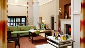 A spacious living area with a green sofa, a dining table set with food and drinks, and a fireplace. - Hilton Garden Inn Rochester/Pittsford (Pittsford)