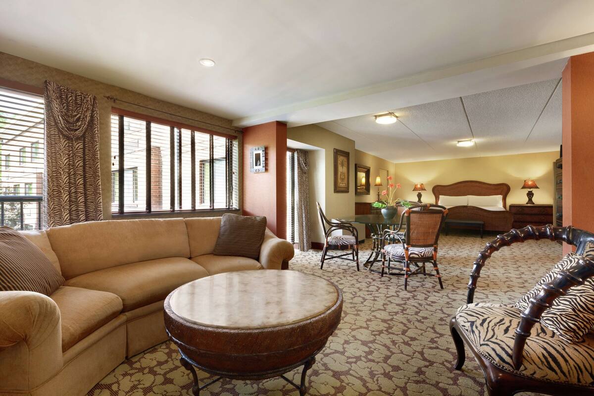 A hotel room with a sofa, round table, zebra-patterned chair, and a bed with a wooden headboard.