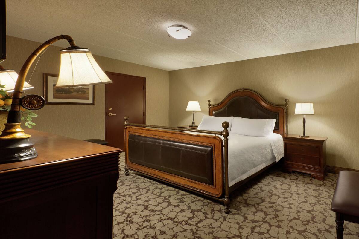 A hotel room with a large bed, two bedside tables with lamps, a wooden dresser, and a patterned carpet.