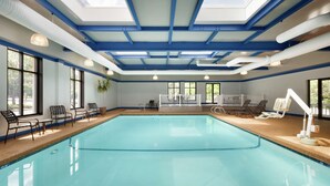 An indoor swimming pool with clear blue water, surrounded by lounge chairs and a sunroofed ceiling. - Hilton Garden Inn Rochester/Pittsford (Pittsford)