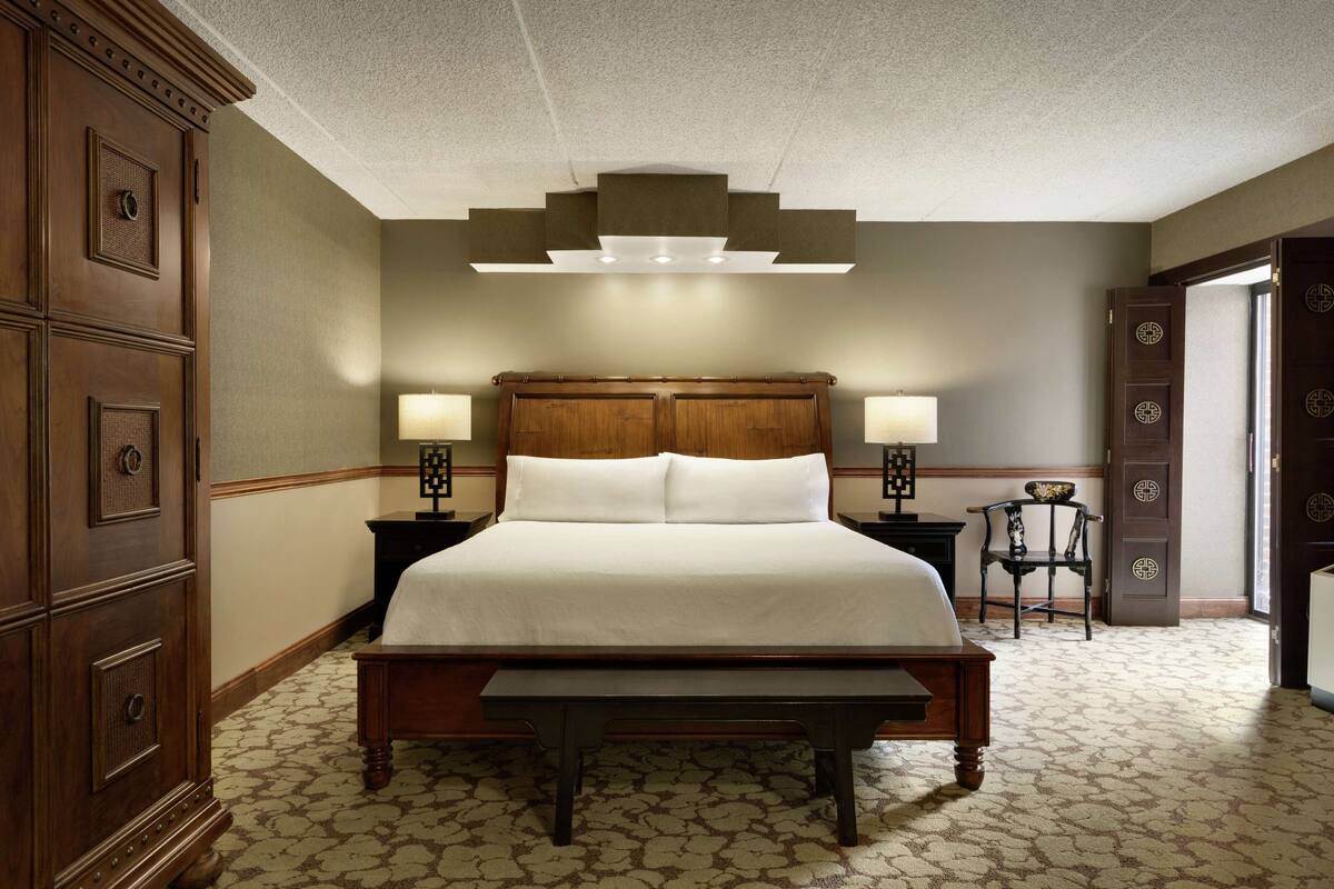 A neatly arranged bedroom with a large bed, two bedside tables, a wooden bench, and a wardrobe.