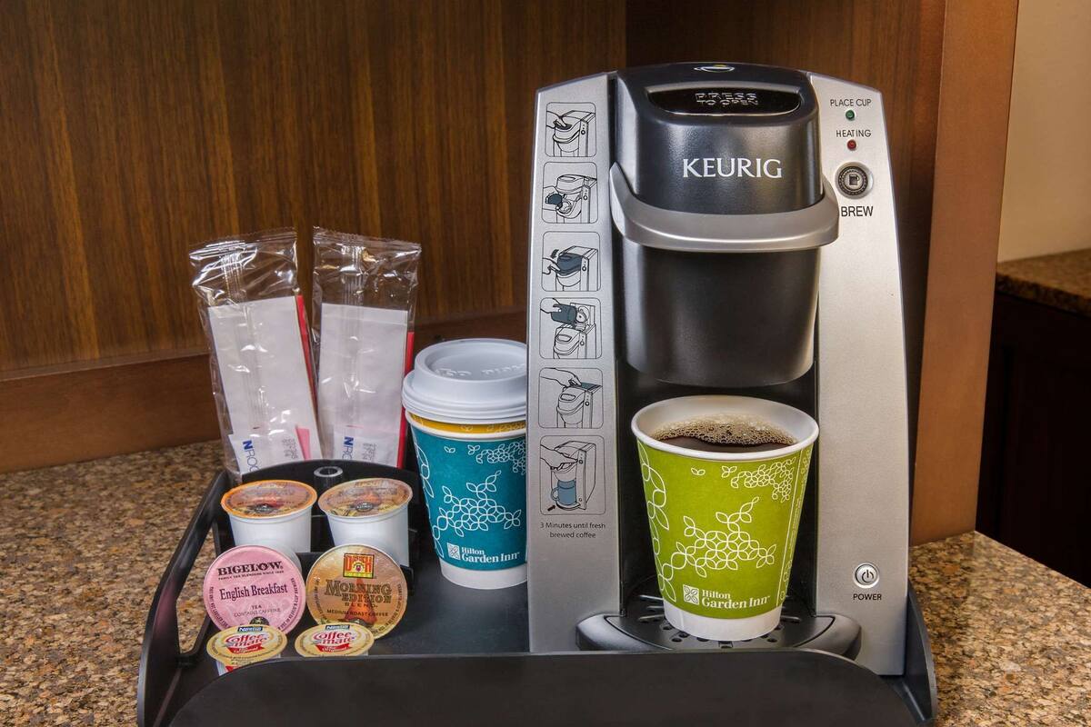 A Keurig coffee maker with a coffee cup and various coffee pods on a tray.