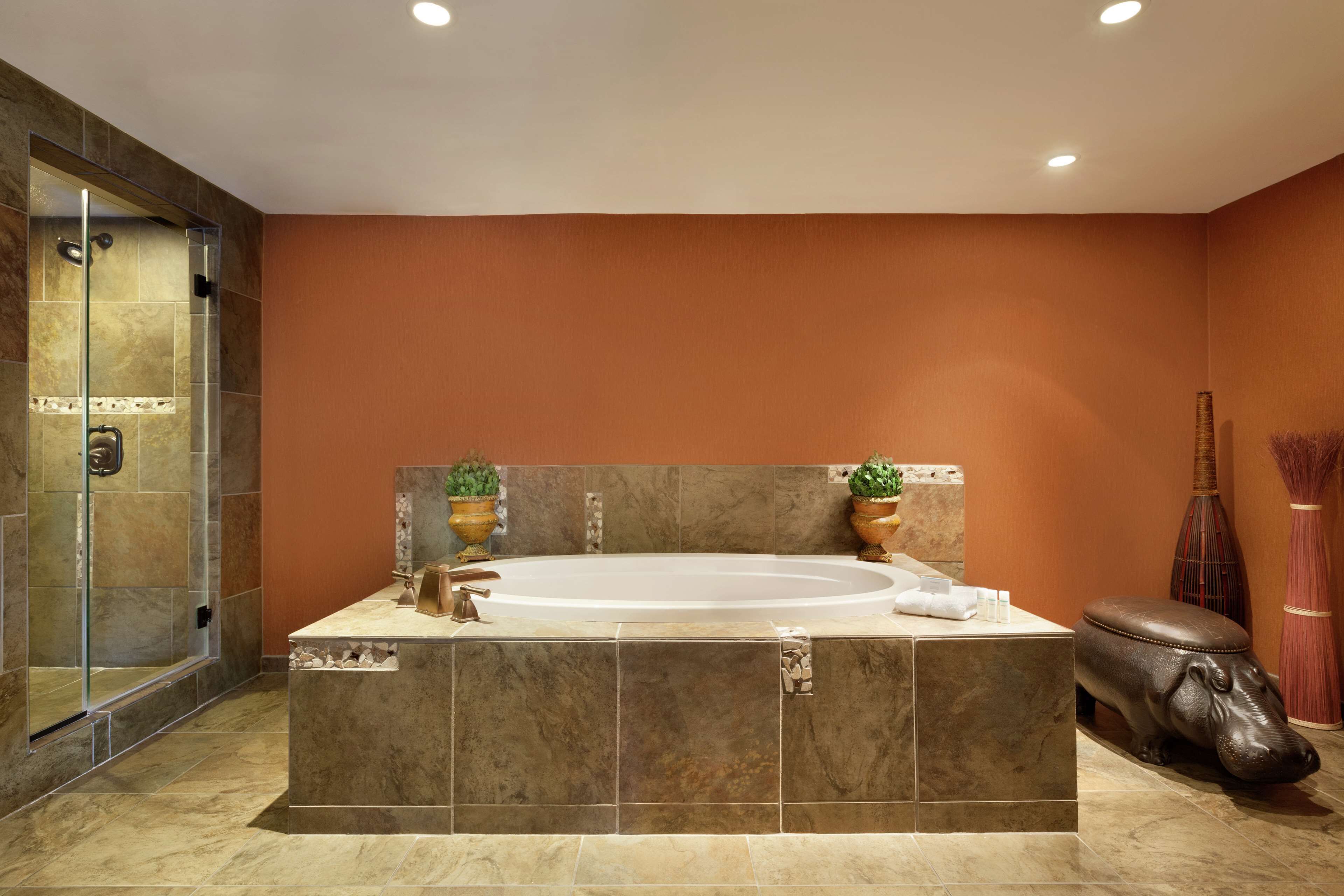 A modern bathroom with a large bathtub, a glass shower enclosure, and a decorative hippo statue.