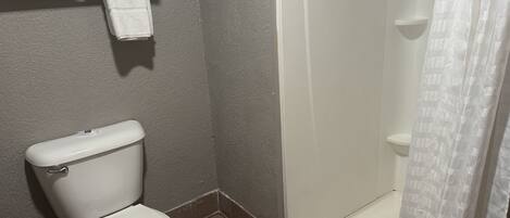 A bathroom with a toilet, a shower, and a towel rack with folded towels.