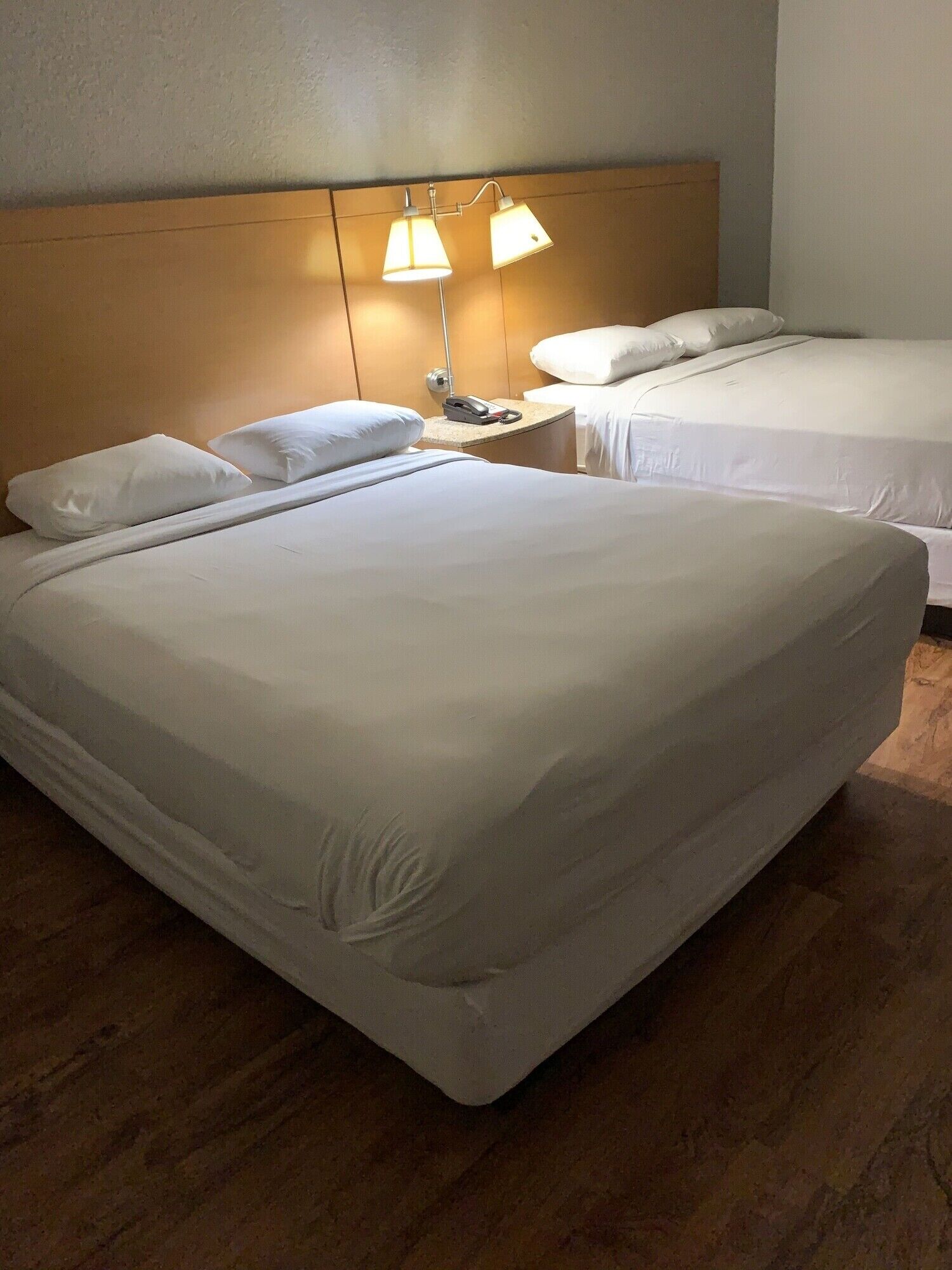 Habitación de hotel con dos camas, cabecero de madera, mesita de noche con lámpara y teléfono.