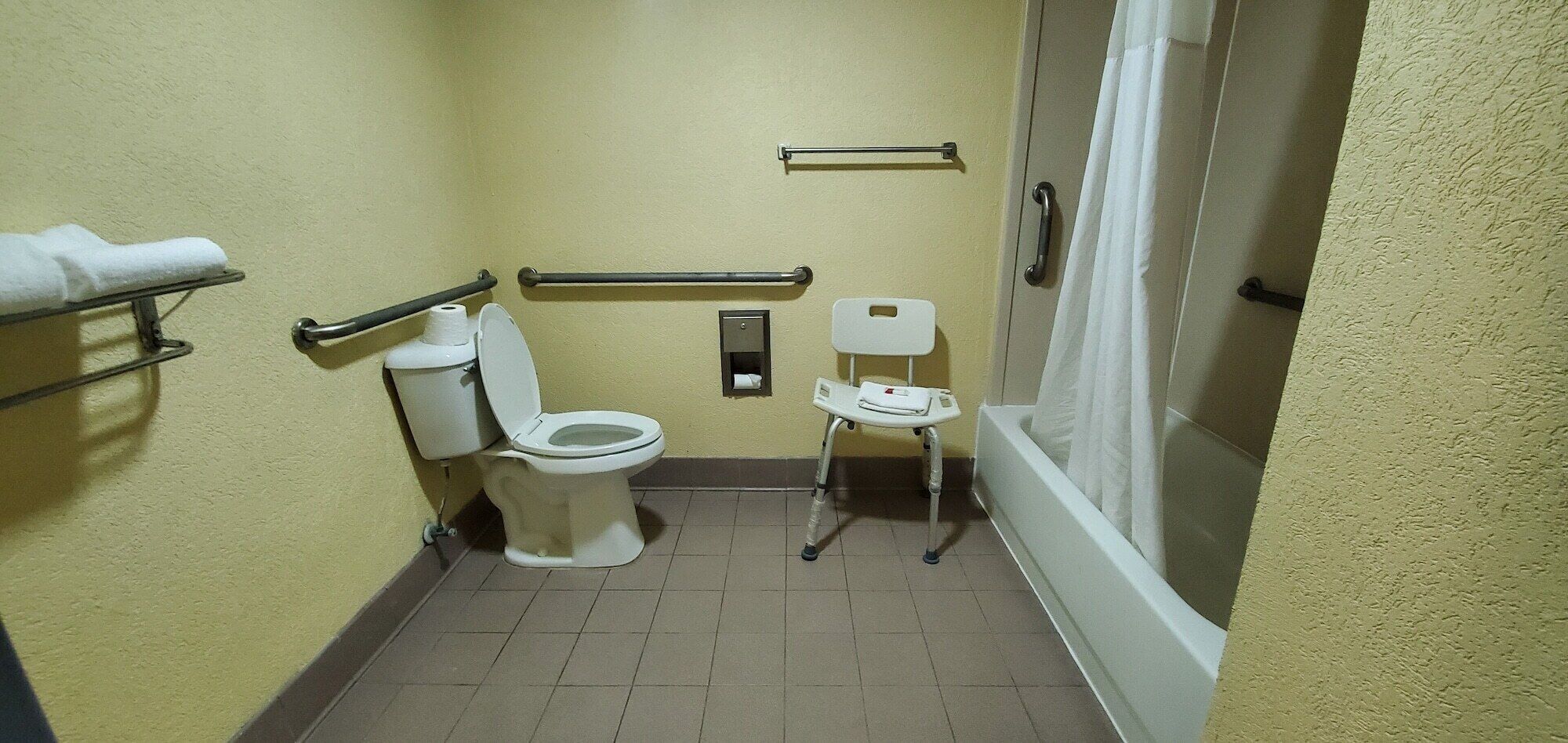 A small bathroom with a toilet, a chair, a towel rack, and a shower curtain.