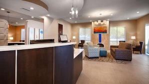 A hotel reception area with a reception desk, seating area with patterned chairs, a fireplace, and a large window providing a view of the outdoors. - Best Western Plus Roswell / Alpharetta (Roswell)