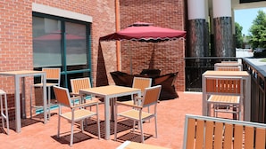 An outdoor patio with brick walls, metal tables and chairs, and a red umbrella. - Best Western Plus Roswell / Alpharetta (Roswell)